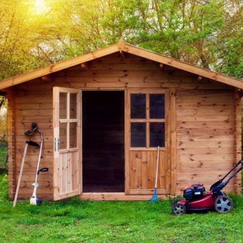 Hovel after work in evening, golden hour. Garden shed (front view) with hoe, string trimmer,  rake and grass-cutter. Gardening tools shed. Garden house on lawn in the sunset. Wooden tool-shed.